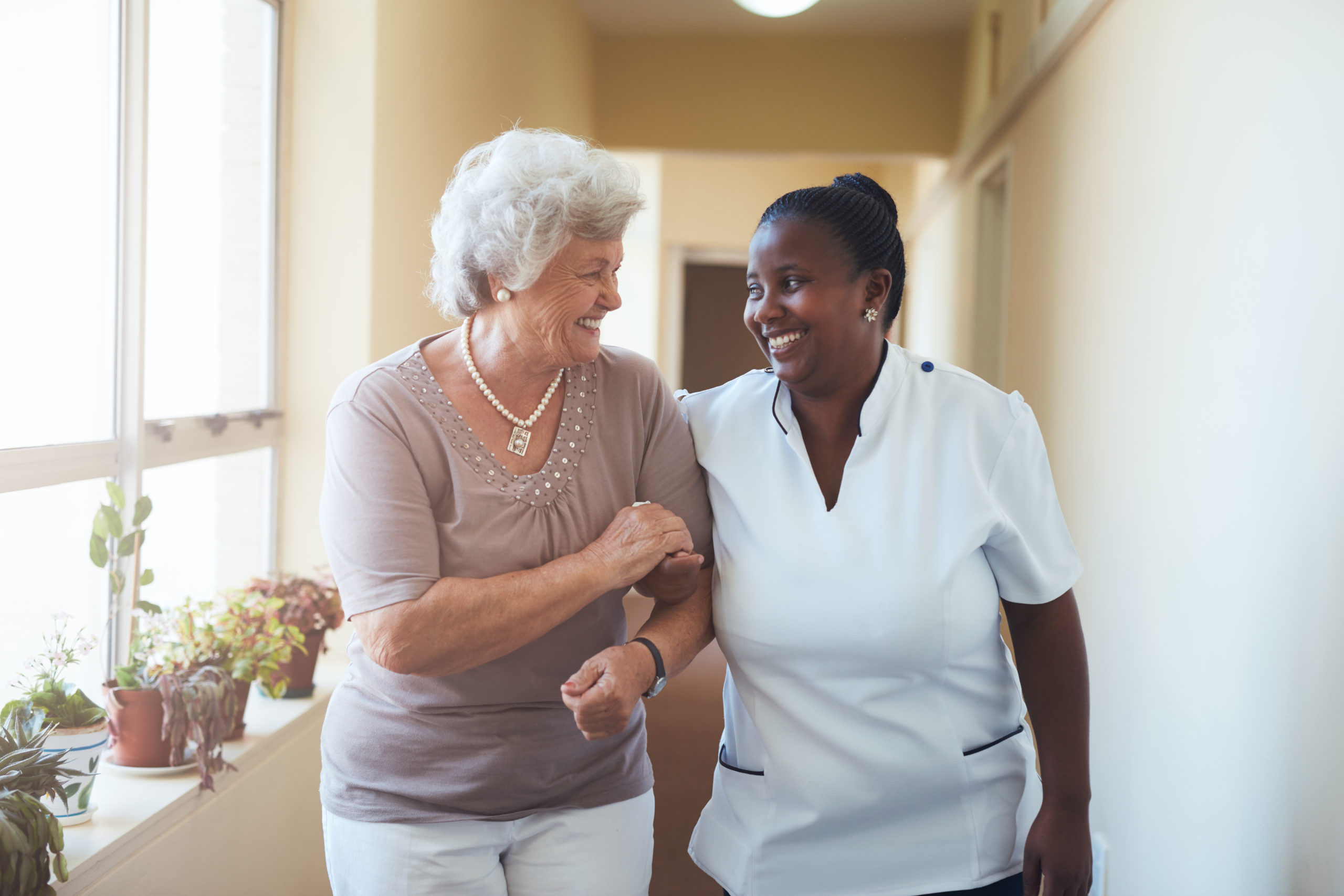 smiling-home-caregiver-and-senior-woman-walking-together